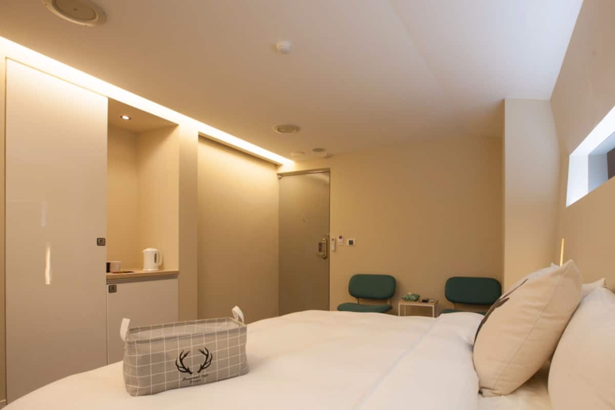 A hotel room with a bed, bedside tables, a mirror, a window, and a bathroom visible through an open door.