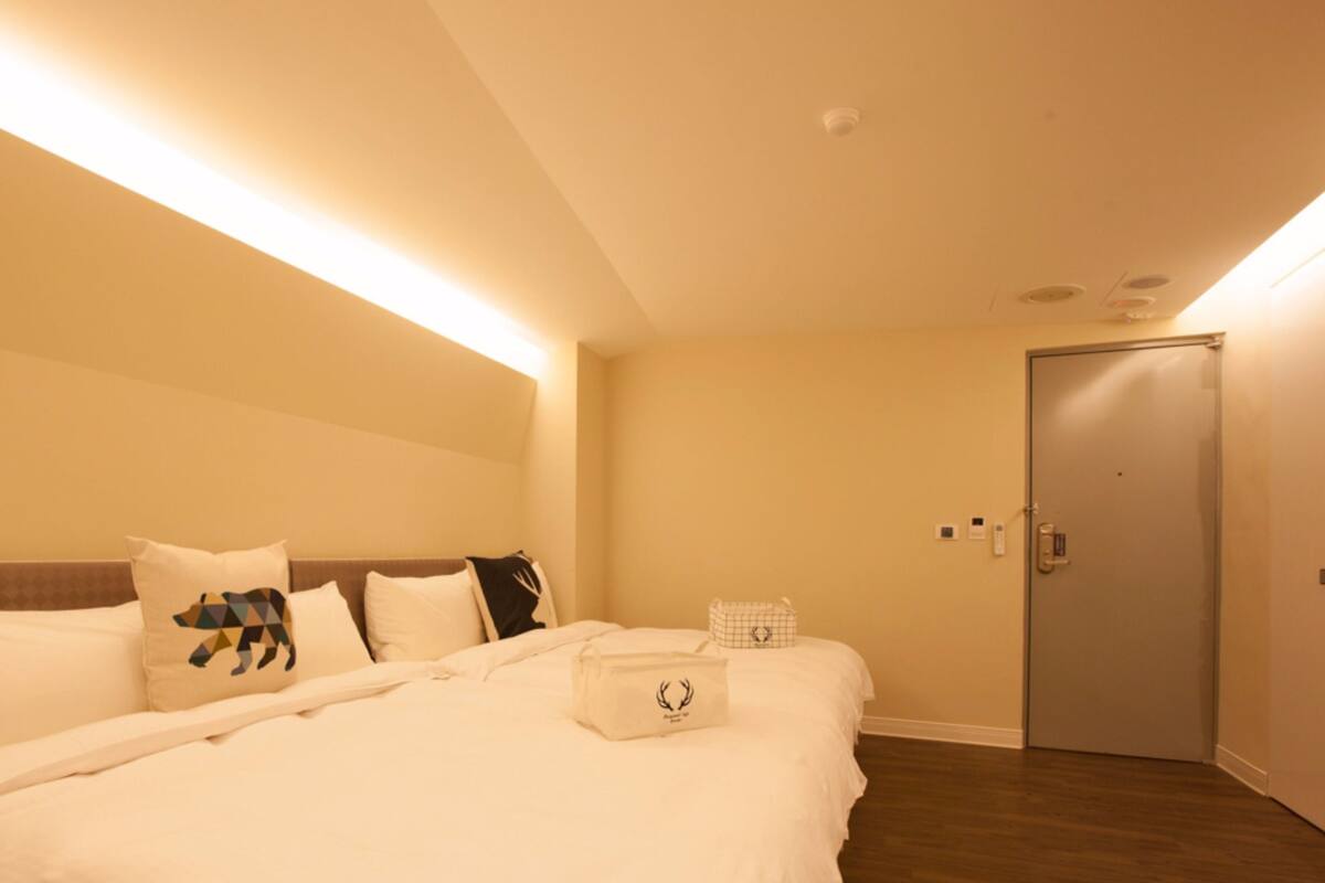 A hotel room with a large bed, a headboard, a bedside table, a nightstand, a door, and a light fixture.