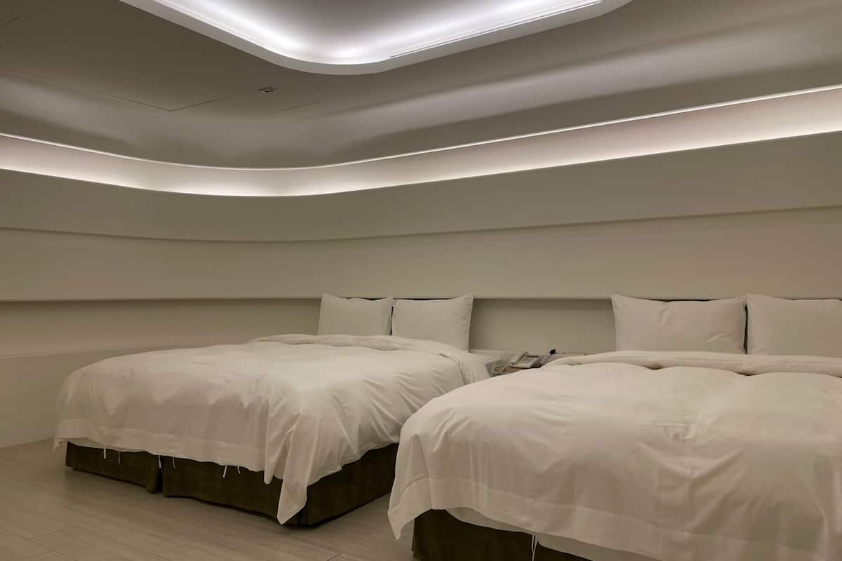 A modern hotel room with two beds, a phone on the nightstand, and a ceiling with recessed lighting.