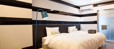 A modern hotel room with a large bed, a desk, a chair, and a floor lamp.