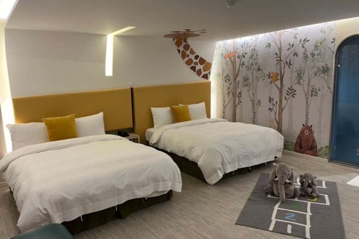 Ein Hotelzimmer mit zwei Betten, einer Wandmalerei mit Giraffen und einer Baummalerei.