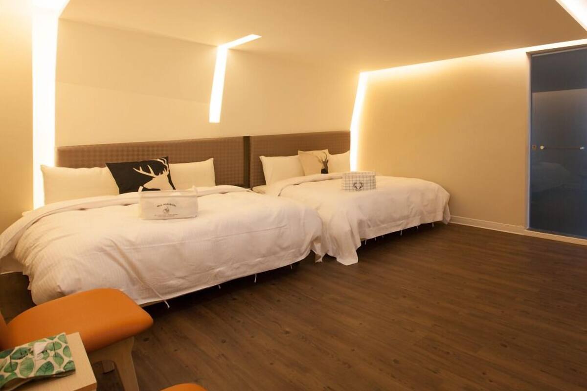 A modern hotel room with two beds, a wooden floor, and a large window.