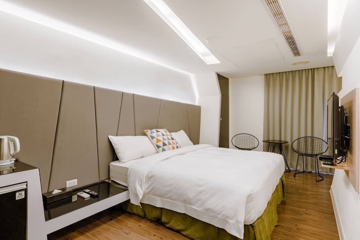 A modern hotel room with a bed, bedside tables, a desk, and a TV.