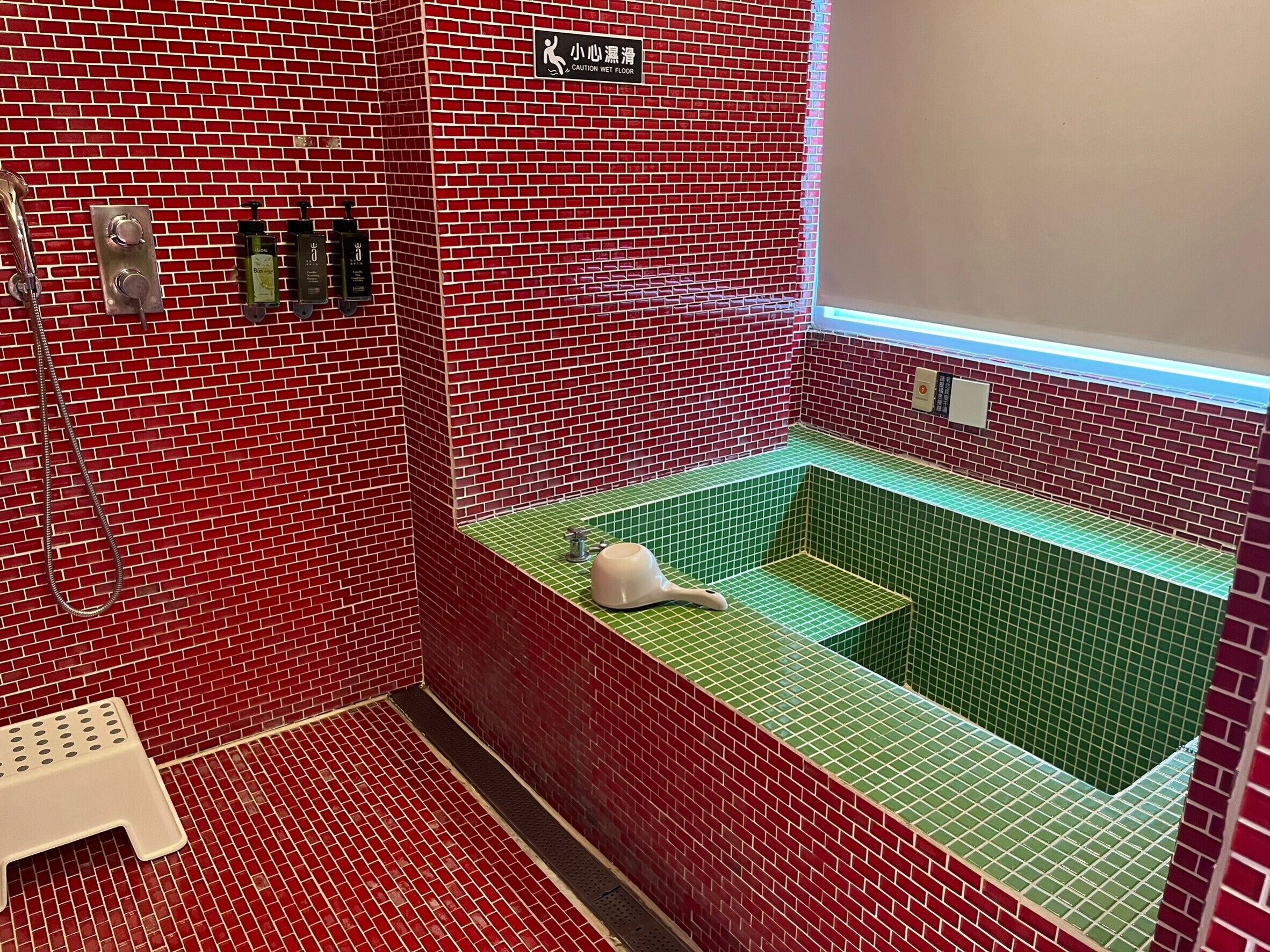 A bathroom with red brick walls, a green tiled sink area, and a caution sign for a wet floor.