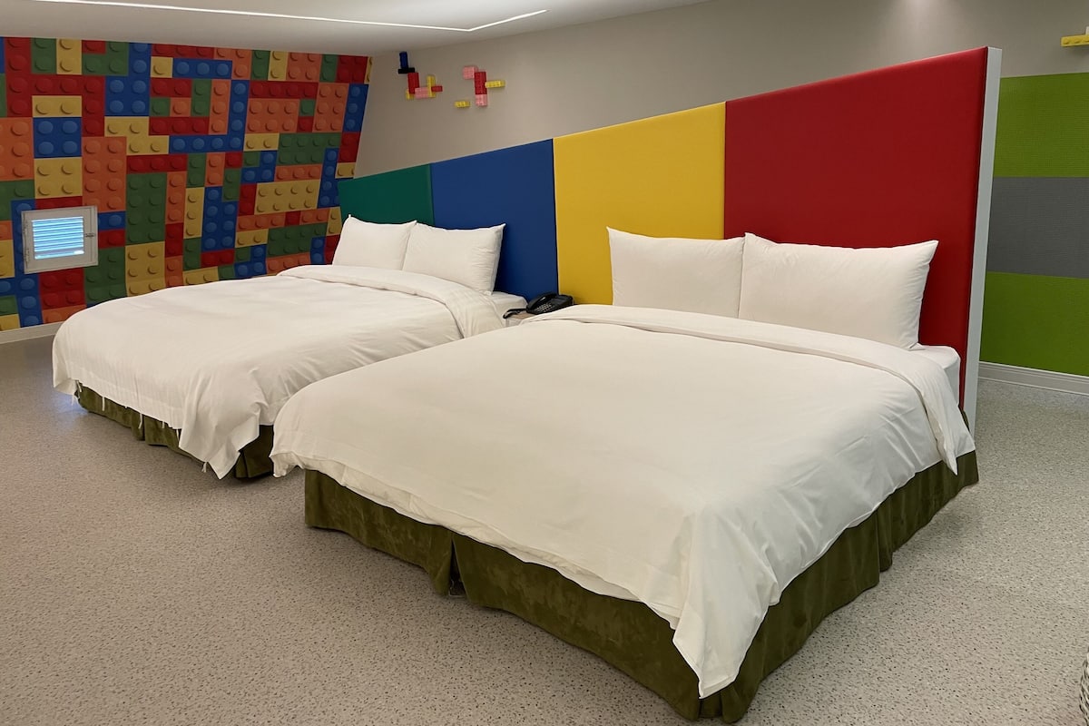 A hotel room with two beds, a colorful wall decoration, and a modern ceiling design.