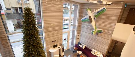 Un interior moderno con un gran árbol de Navidad, una zona de estar con un sofá y sillones, y una exhibición de modelos de aviones.