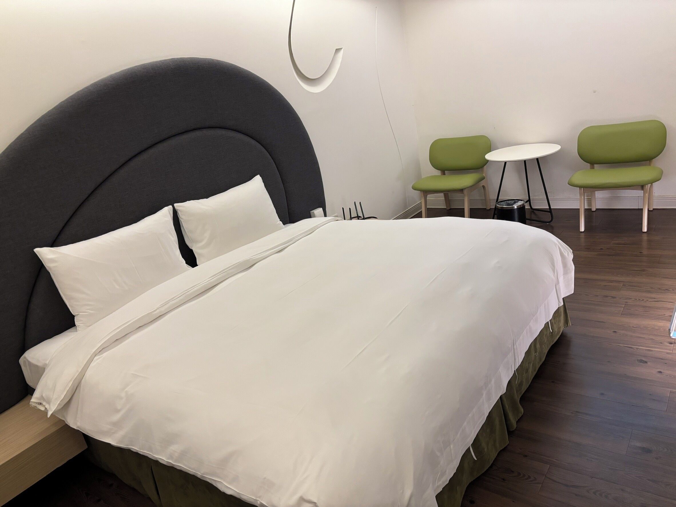 A modern hotel room with a large bed, green chairs, and a small table.