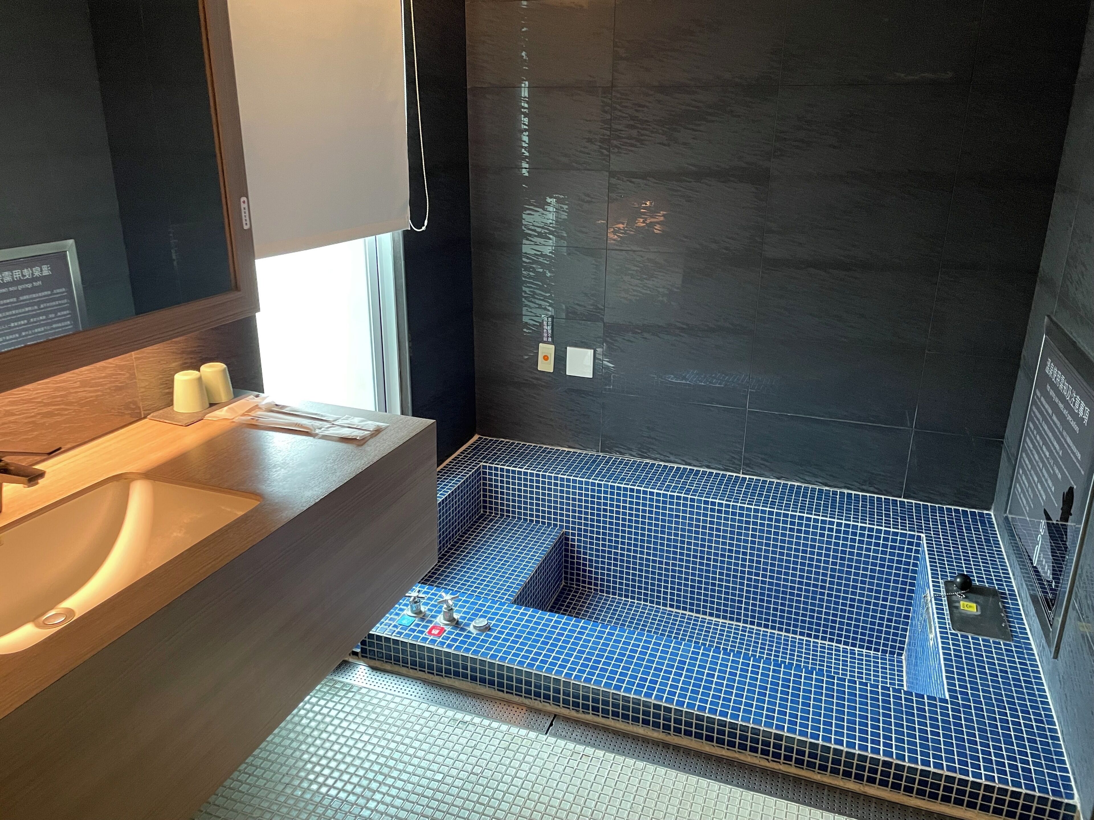 Un baño moderno con tocador de madera, un espejo grande y una zona de ducha con azulejos azules.