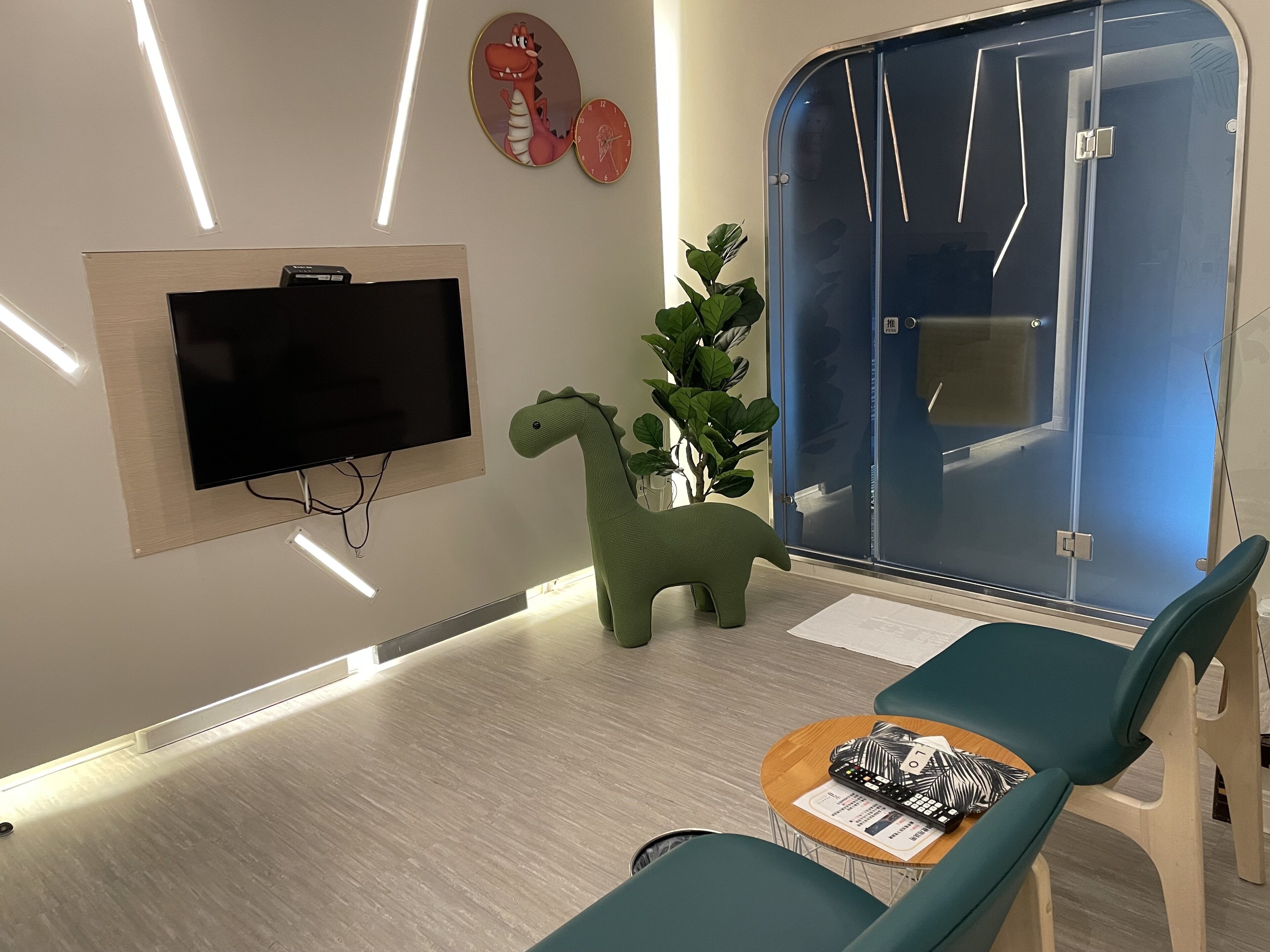 A modern waiting area with a flat-screen TV, a green dinosaur toy, and a blue door.