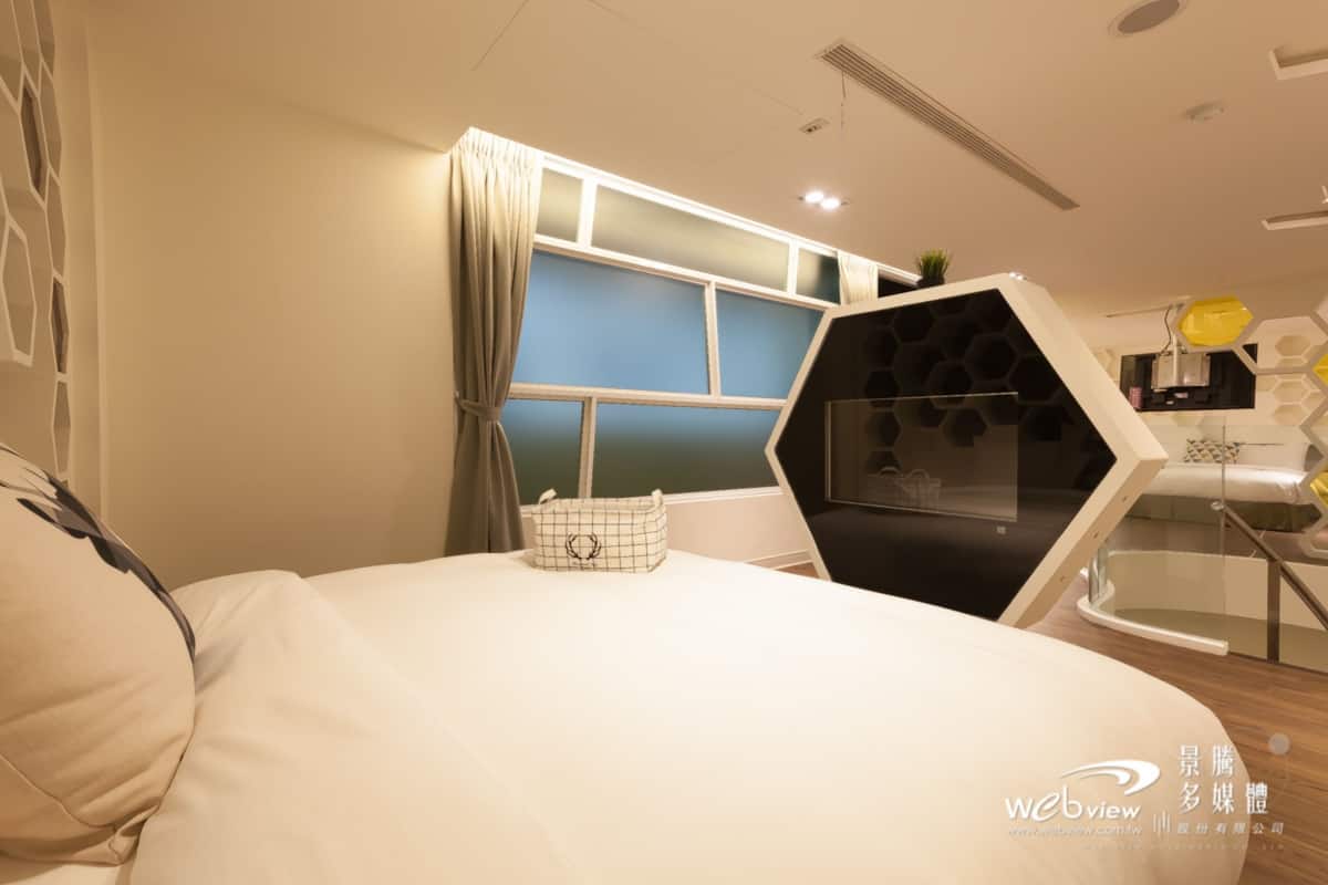 A modern bedroom with a large bed, a geometric wall unit, and a view of the kitchen area.