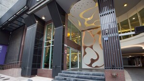 Entrada moderna de un edificio con amplios ventanales, un muro decorativo y una escalera que lleva a la entrada.