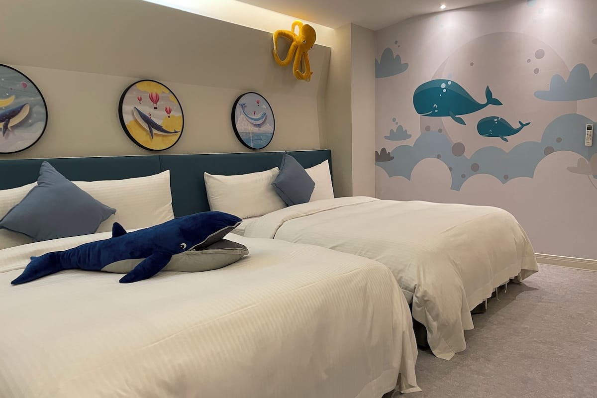 A bedroom with two beds, a plush toy, and wall art depicting whales and hot air balloons.