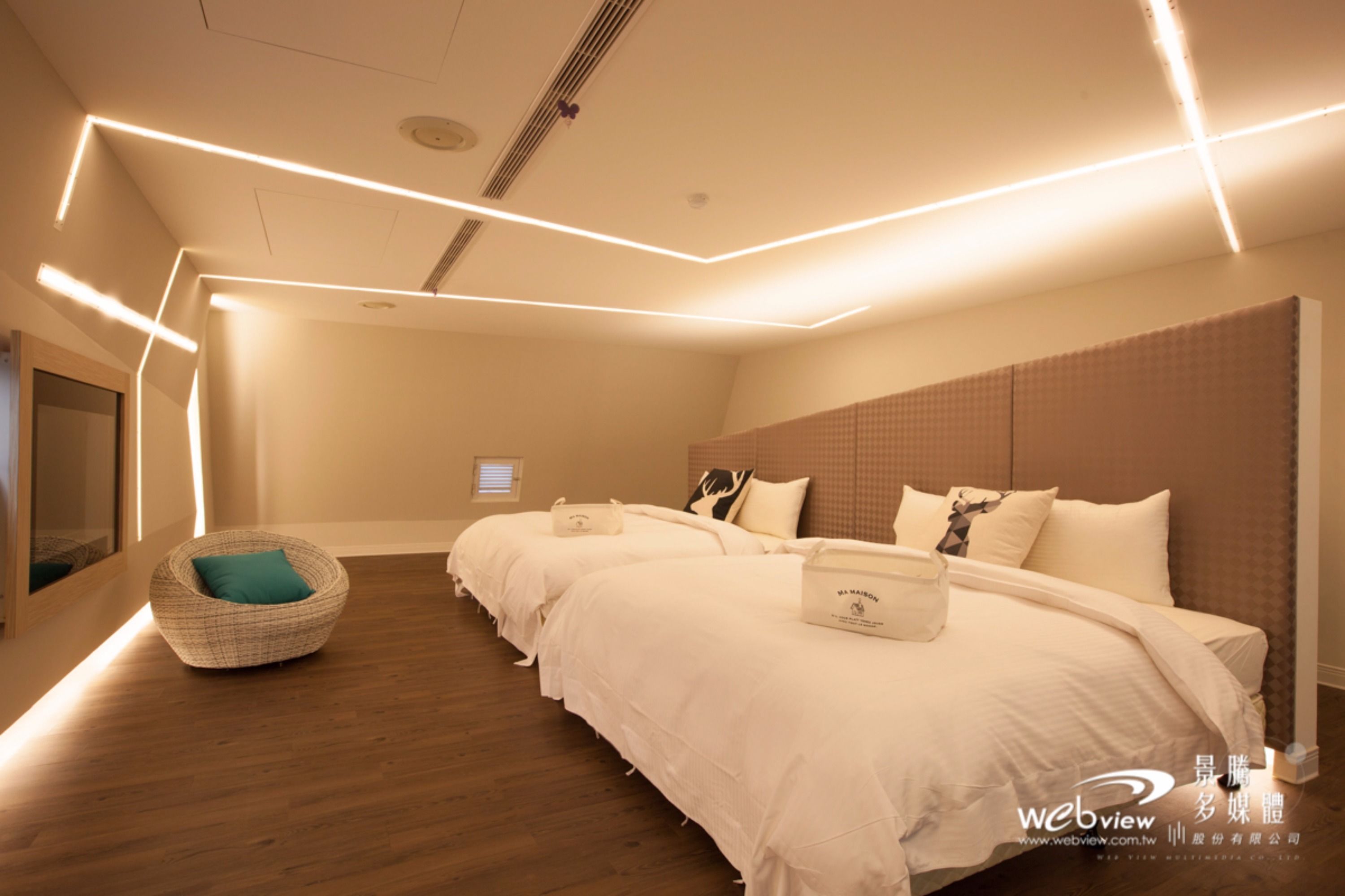 A hotel room with two beds, a wooden floor, and modern lighting.