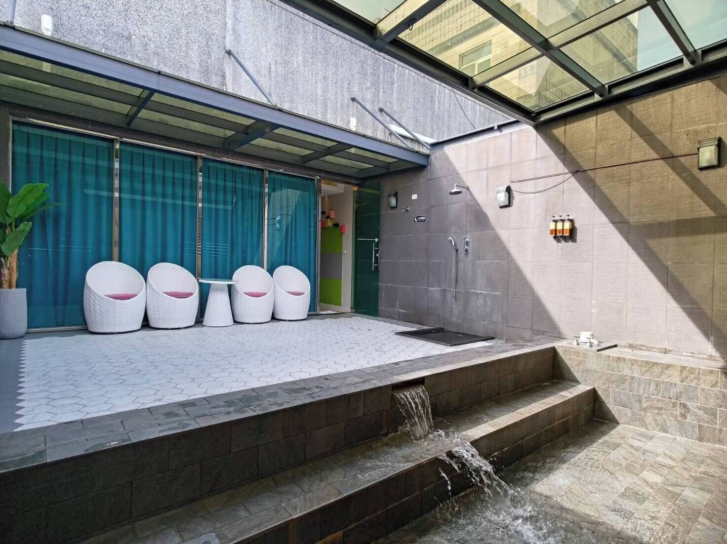 A modern outdoor area with a seating arrangement, a water feature, and a glass ceiling structure.