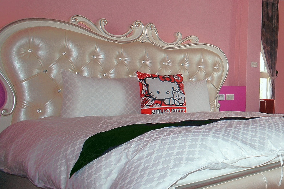 A bedroom with a tufted headboard, a Hello Kitty pillow, and pink walls.