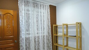 A room with a wooden door, a lace curtain, and a wooden shelf unit against a wall. - Bukit Tinggi Klang - Cozy Home (Klang)