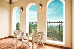 A balcony with two wicker chairs and a small table, overlooking a lush green landscape through a metal railing. - Sungsan Paradise Hill (Seogwipo)
