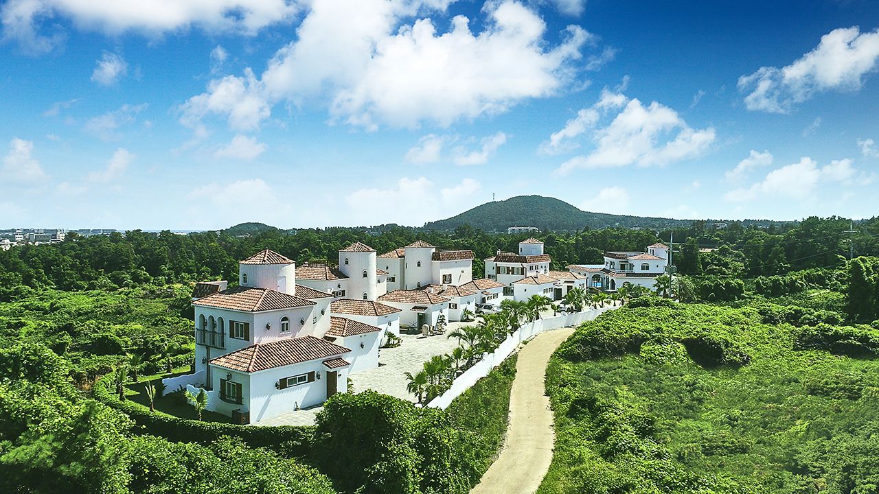 Uma vila costeira com edifícios brancos, uma estrada sinuosa e uma montanha ao fundo.