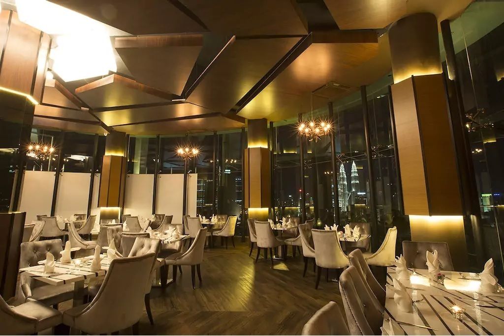 A modern dining area with tables set for service, large windows offering city views, and contemporary lighting fixtures.