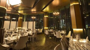 A modern dining area with tables set for service, large windows offering city views, and contemporary lighting fixtures. - Wong's Homestay at Regalia Residence (Kuala Lumpur)