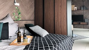 A modern bedroom with a herringbone-patterned wall, a bed with a black and white geometric bedspread, and a bedside table with a tray of wine bottles and glasses. - Wong's Homestay at Regalia Residence (Kuala Lumpur)