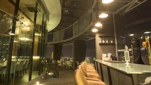 A modern restaurant with a bar area, glass walls, and a view of the cityscape. - Wong's Homestay at Regalia Residence (Kuala Lumpur)