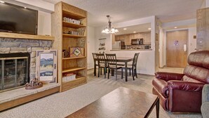 A living room with a fireplace, wooden shelves, a dining area with a chandelier, and a leather armchair. - VS643 and 645H Village Square (Copper Mountain)