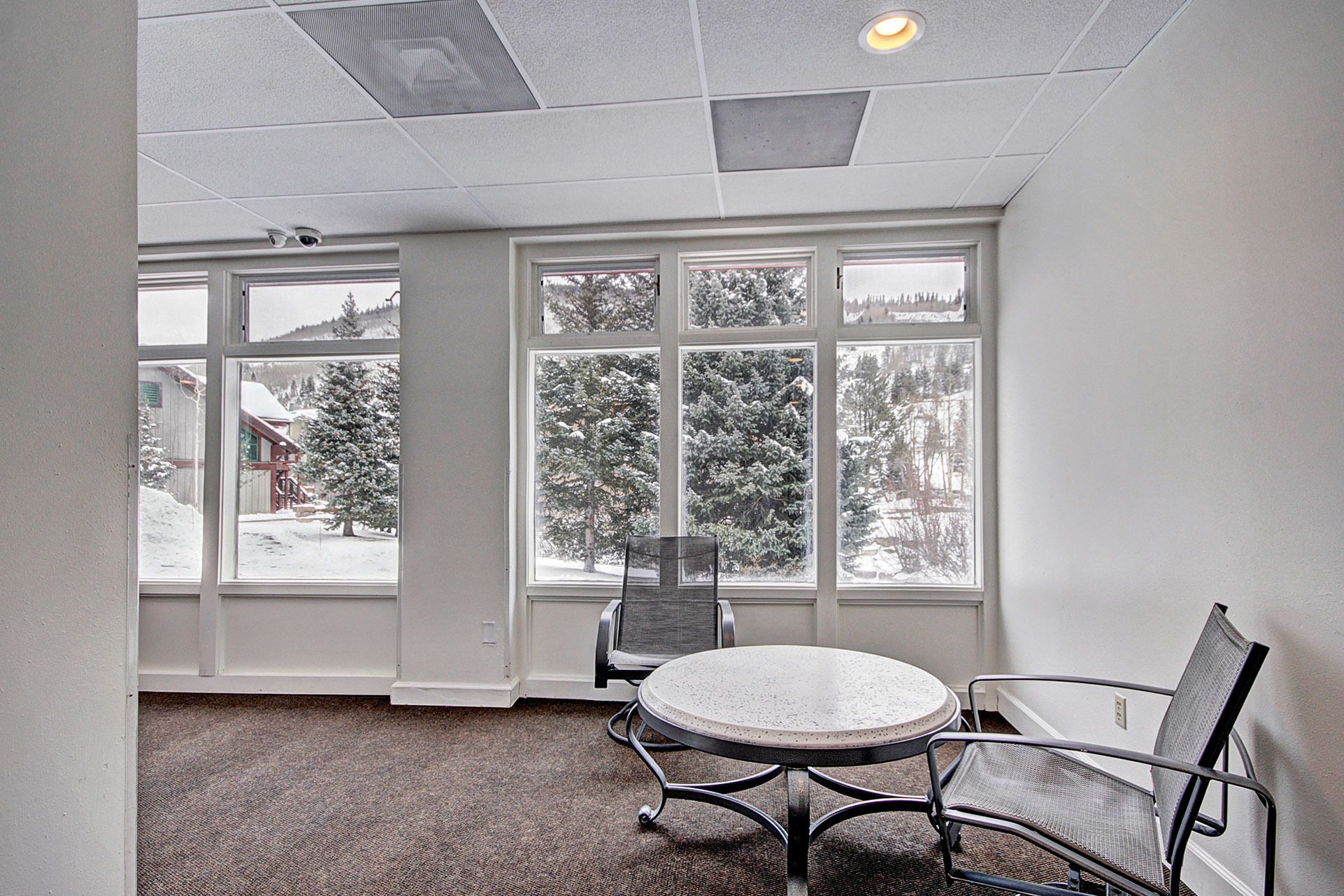 A conference room with a round table and two chairs, large windows with a view of snow-covered trees and a building.