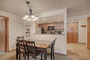 A dining area with a wooden table and chairs, a hanging light fixture, and a kitchen in the background. - VS643 and 641H Village Square (Copper Mountain)