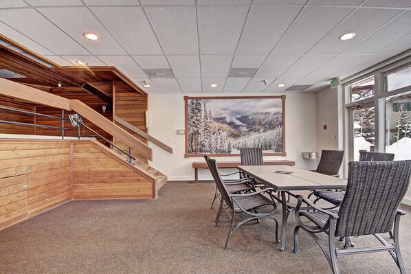 Uma sala de conferências com uma grande mesa e cadeiras, uma escada com guarda-corpo de madeira e uma janela ampla com vista para a montanha.