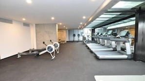 A gym with multiple treadmills and stationary bikes, a grey carpeted floor, and a modern design with a glass ceiling. - Southern Cross CBD Apartment (Melbourne)