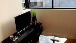 A modern living room with a flat-screen TV on a black stand, a glass coffee table, and a small potted plant. - Southern Cross CBD Apartment (Melbourne)