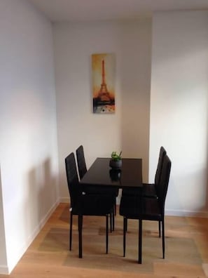 A dining area with a black table and chairs, a small plant on the table, and a painting of the Eiffel Tower on the wall. - Southern Cross CBD Apartment (Melbourne)