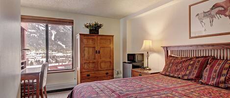 Une chambre à coucher avec un grand lit, une armoire en bois, un bureau avec une chaise, une lampe et un téléviseur.