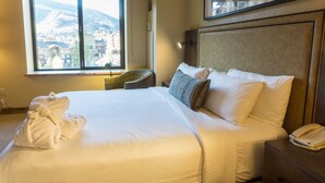 Ein Hotelzimmer mit einem großen Bett, einem Nachttischtelefon und Blick auf einen Berg durch ein Fenster.