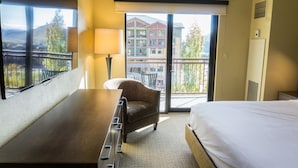 A hotel room with a bed, a desk, a chair, a balcony with a view of buildings and mountains. - Rustice Conod with Modern Kitchen  Facilities by RedAwning (Park City)