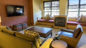A living room with a sofa, a coffee table, a fireplace, and a television mounted on the wall.