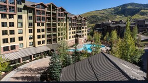 A multi-story hotel with a swimming pool, surrounded by trees and a mountain backdrop.