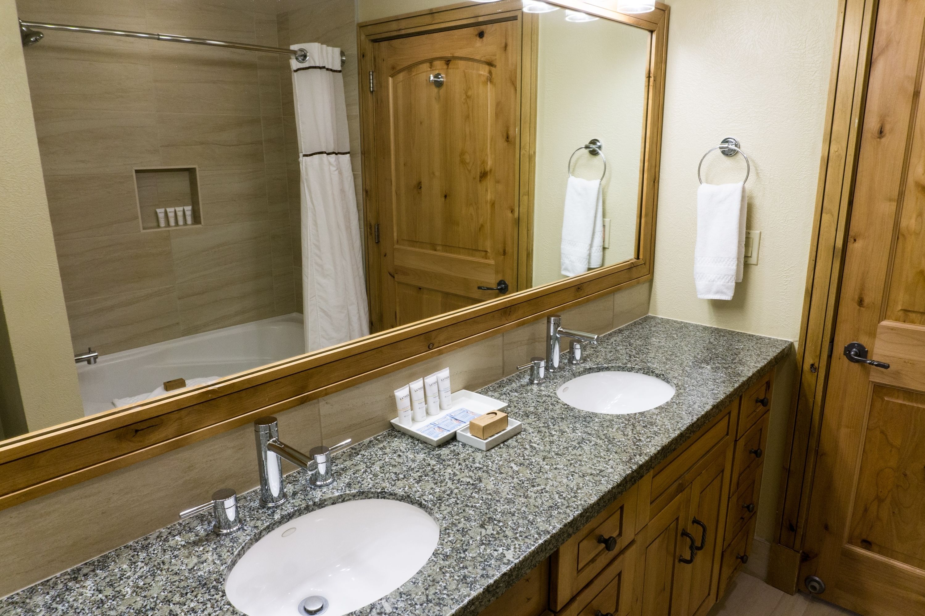 Une salle de bain avec deux lavabos, un grand miroir, des meubles en bois et un espace douche.