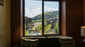 Quarto com uma grande janela com vista para uma região montanhosa, com edifícios e piscina.
