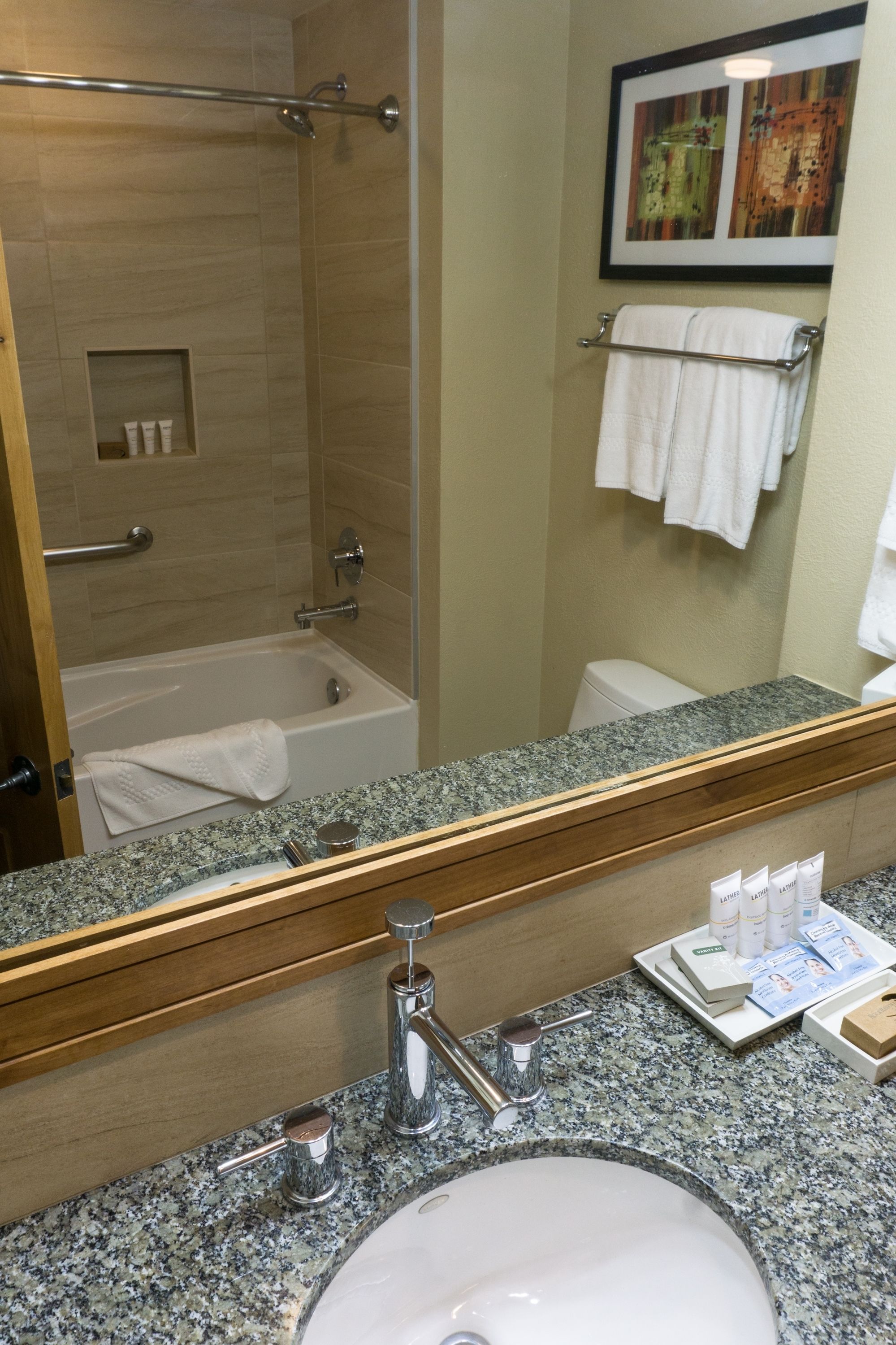 A bathroom with a granite countertop, a sink, a mirror, a shower, and a towel rack.