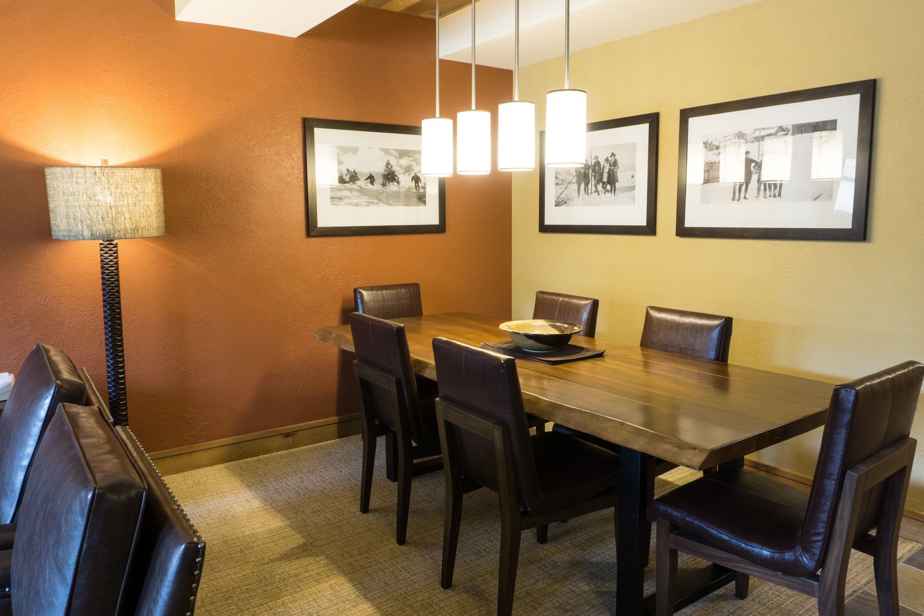 A dining area with a wooden table, six chairs, a bowl, and framed pictures on the wall.