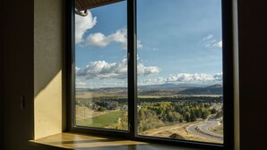 Une vue depuis une fenêtre donnant sur une route sinueuse, un champ verdoyant et des montagnes lointaines.