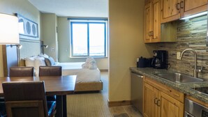 Une chambre d’hôtel compacte dotée d’une kitchenette, d’un coin repas, d’un lit avec vue et d’une grande fenêtre.