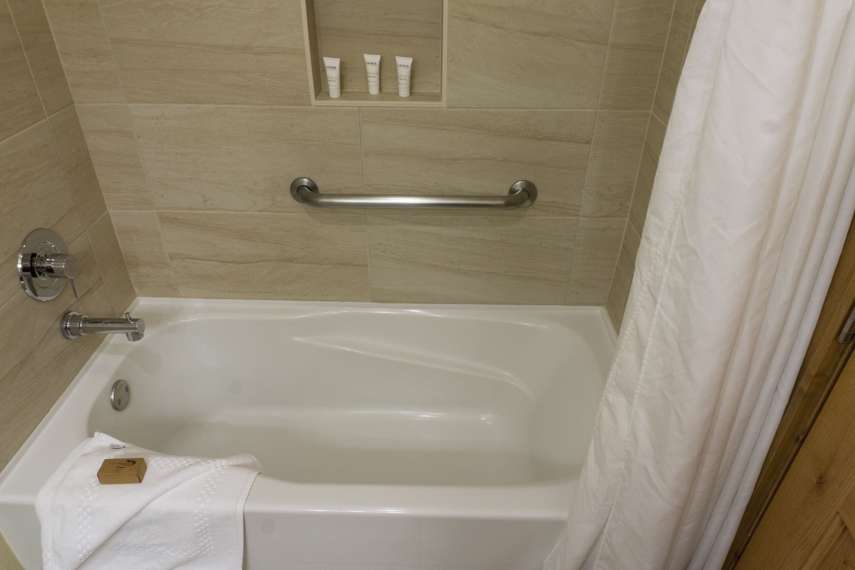 A bathtub with a grab bar, a towel, and toiletries in a shower area.