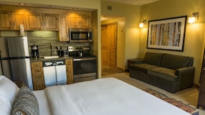 A hotel room with a bed, a sofa, a kitchenette with a refrigerator, microwave, stove, and coffee maker.
