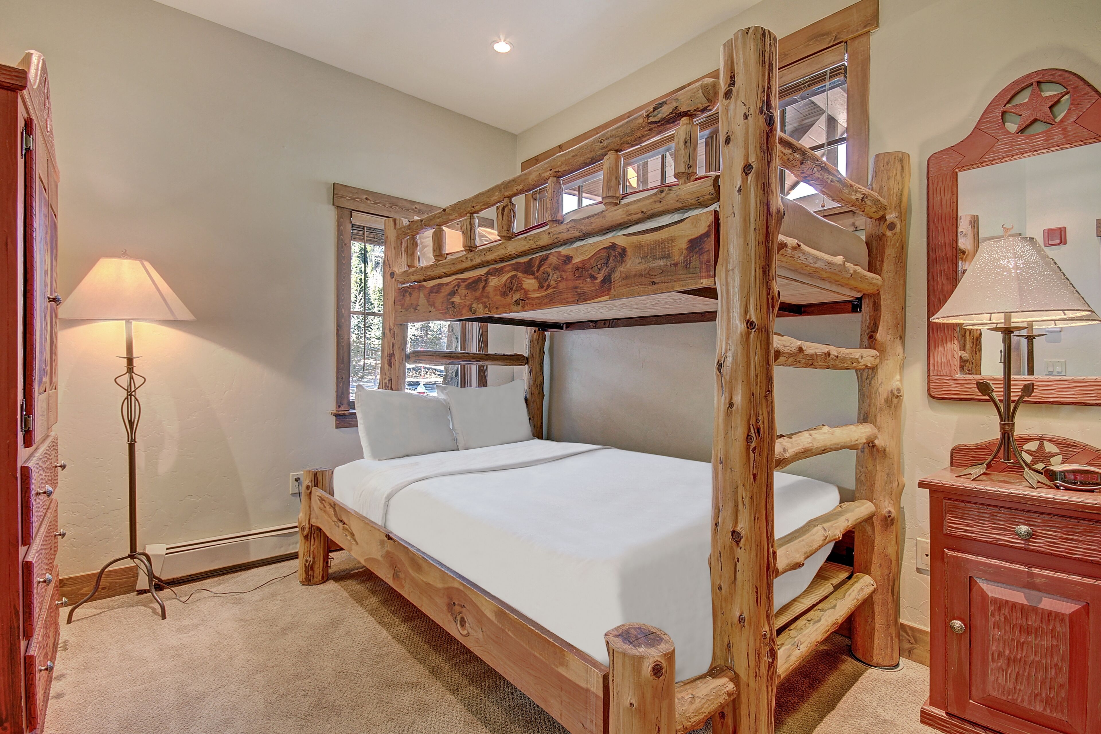 A bunk bed with a wooden frame, a bedside lamp, and a dresser with a mirror.