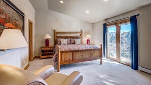 A bedroom with a large bed, a wooden headboard, a nightstand, a lamp, a chair, and a large window with curtains. - Streamside 333B (Frisco)