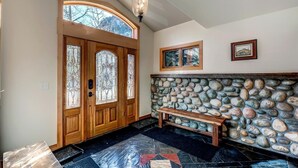 A wooden front door with stained glass panels, a stone wall with a bench, and a ceiling light fixture. - Streamside 333B (Frisco)