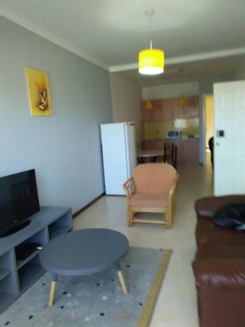 A living room with a television, a sofa, a dining table, and a kitchen in the background.